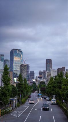 cars are driving down the road in front of tall buildings and skyscrapers on a cloudy day