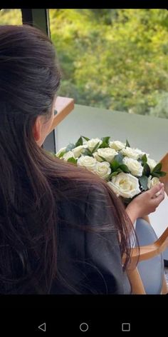 a woman sitting in a chair holding a bouquet of white roses