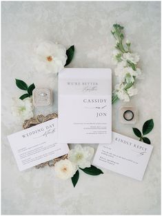 the wedding stationery is surrounded by flowers and rings