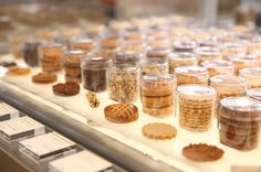 many jars filled with different types of cookies on display in a glass case at a bakery