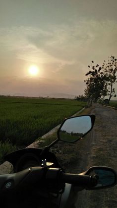 a motorcycle parked on the side of a dirt road next to a lush green field