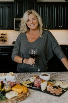 a woman standing in front of a table filled with food and glasses of red wine