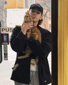 a woman holding a cat in her hands while standing next to a bus door on the street