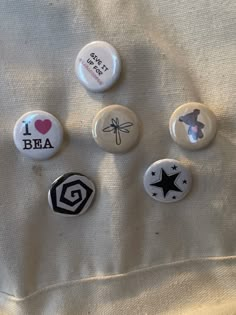 six buttons with different designs on them sitting on a white cloth covered bed sheet in the sunlight