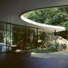 the inside of a house with glass walls and large rocks in front of it, surrounded by greenery