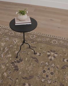 a small table with a book on top of it next to a rug and potted plant