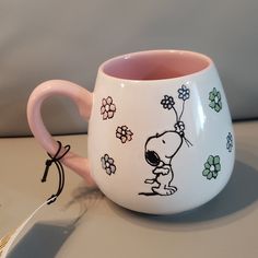 a pink and white coffee cup with a snoopy cartoon on it