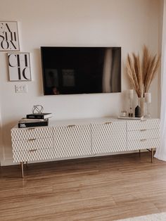 a flat screen tv mounted on the wall above a white dresser in a living room