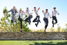 a group of men jumping in the air on top of a stone wall with trees