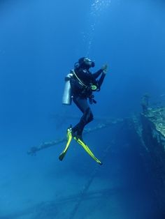 a person in scuba gear is diving over the ocean with a boat wreck behind them