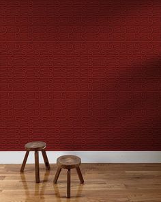 two stools in front of a red wall with an intricate pattern on it, against a wooden floor