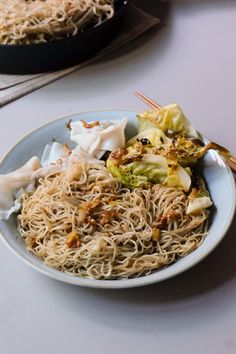 a plate of noodles and vegetables on a table with chopsticks next to it