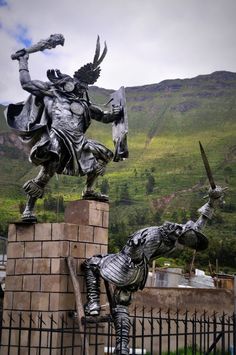 a statue of a knight on top of a brick pillar with two swords in his hand