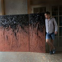 a man is standing next to a large piece of art that looks like rocks and dirt