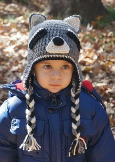 a little boy wearing a crocheted hat with a raccoon on it