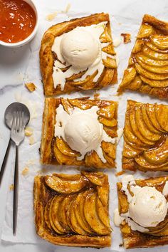 four pieces of apple tart with ice cream on top and two spoons next to it