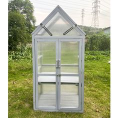 a small white greenhouse sitting on top of a green grass covered field with power lines in the background