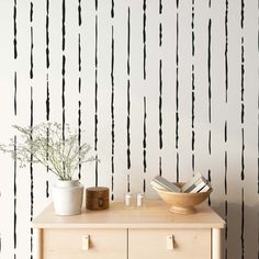 a wooden table topped with a vase filled with flowers next to a wall covered in black and white stripes