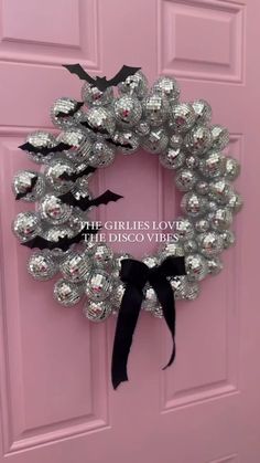 a pink door with a black bow on it and a silver wreath hanging from the front