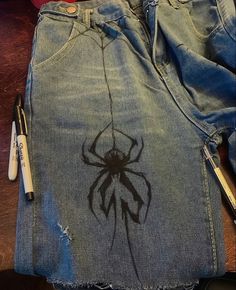 a pair of ripped jeans with a spider drawn on the side and writing utensils next to it