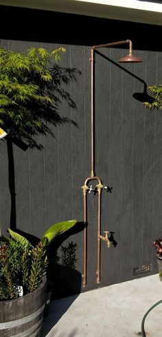 an outdoor shower in front of a black wall and potted plants on the side