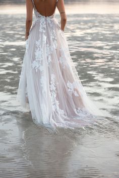 a woman standing in the water wearing a white dress with flowers on it's back