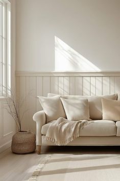 a living room with a white couch and some pillows on the floor next to a potted plant