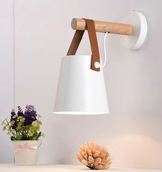 a white lamp hanging from the side of a wall next to a potted plant