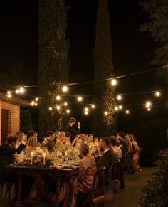 a group of people sitting around a table with food and drinks on it at night