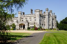 a large castle like building sitting in the middle of a lush green field next to a road