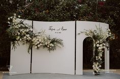 an outdoor ceremony setup with white flowers and greenery on the wall, surrounded by trees