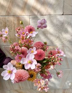 a person holding a bouquet of flowers in front of a brick wall with shadows on it