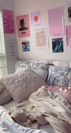 an unmade bed with pink and white sheets, pillows and pictures on the wall