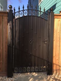 an iron gate in front of a blue house with wood fence and stone path leading to it