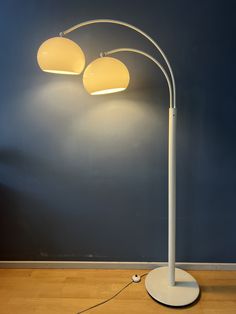 a white floor lamp with three lamps on it in front of a blue painted wall