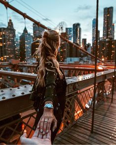 a woman holding the hand of another person on top of a bridge in new york city