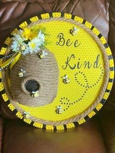 a yellow and black sign that says bee kind with flowers in it on a brown leather chair