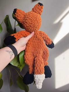 a hand holding an orange and black stuffed animal on top of a green leafy plant