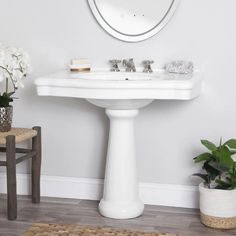 a white pedestal sink sitting next to a mirror and potted plant in a room