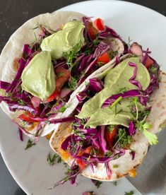 two tacos on a white plate with avocado and red cabbage slaw