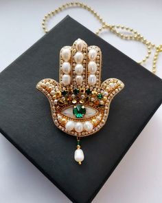 a gold and green hamsa necklace with pearls on it's side, resting on a black book