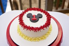 a mickey mouse birthday cake with red and yellow icing on a white tablecloth