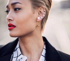 a close up of a person wearing earrings and a suit with red lipstick on her lips