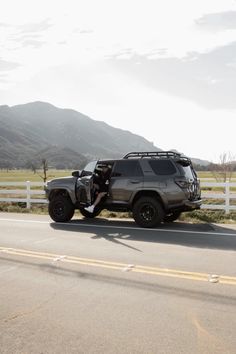 a jeep driving down the road next to a white fence