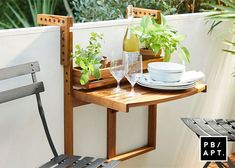 an outdoor table with two chairs and a wine glass on it next to a wall