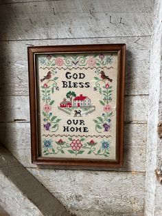 a cross - stitch sample hanging on the side of a wooden wall, with words that read god bless our home