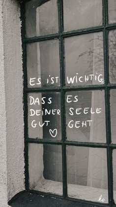 a window with writing written on it in front of a white wall and black frame