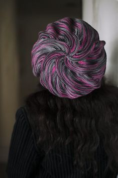 a woman with long curly hair wearing a purple and black knitted hat on top of her head