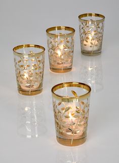 four glass candles with gold leaf designs on the top and bottom, all lit up