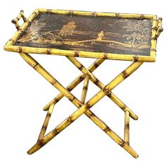 a bamboo table with a painting on it's top and two legs that are crossed together